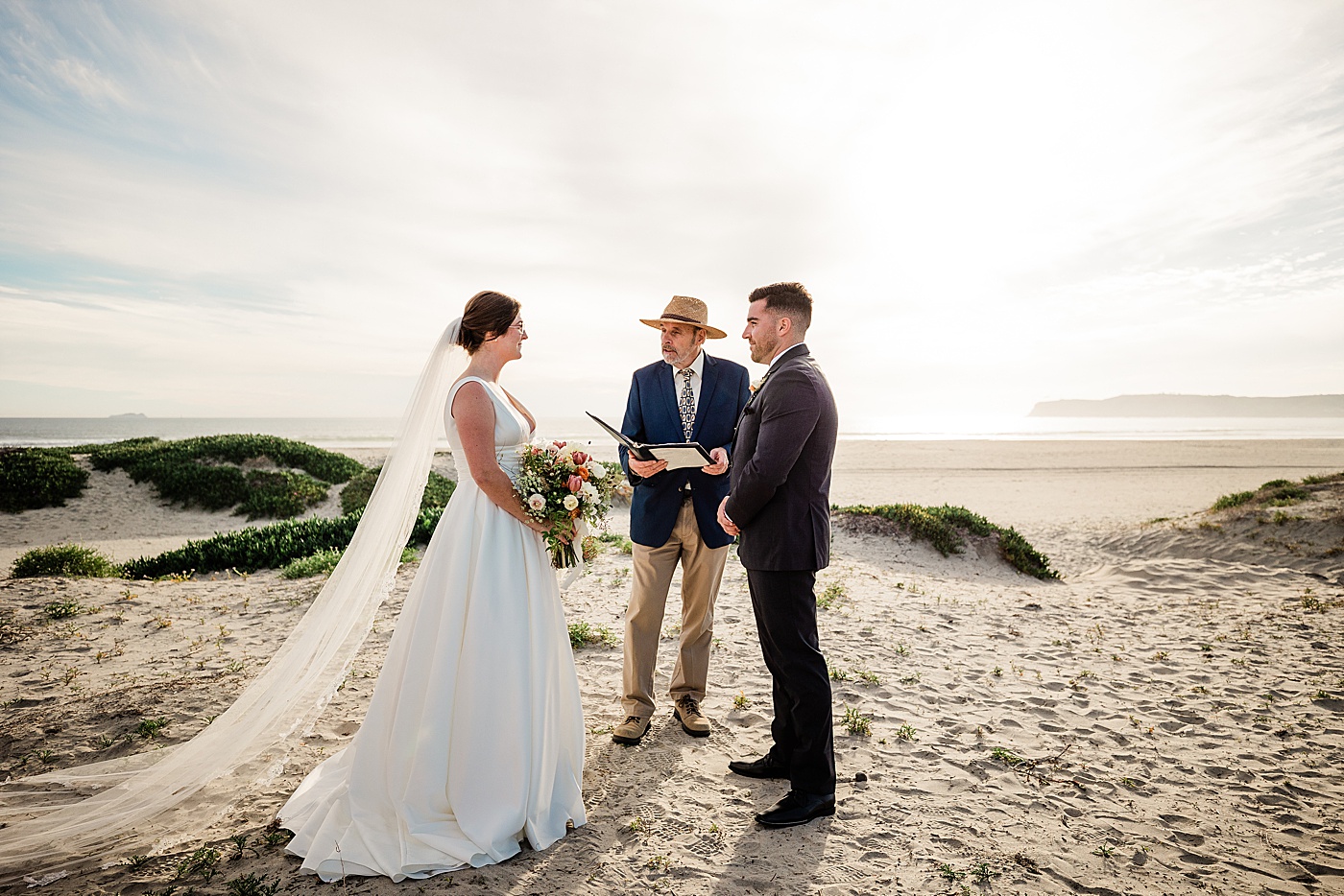 Coronado Beach elopement ceremony with bride, groom, and officiant at the dunes.