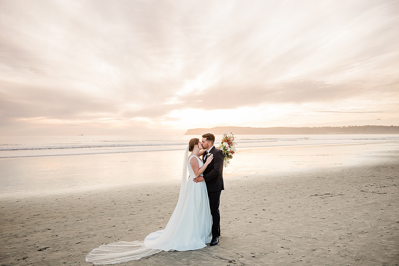Coronado beach elopement at sunset. Bride and groom embracing at the beach.