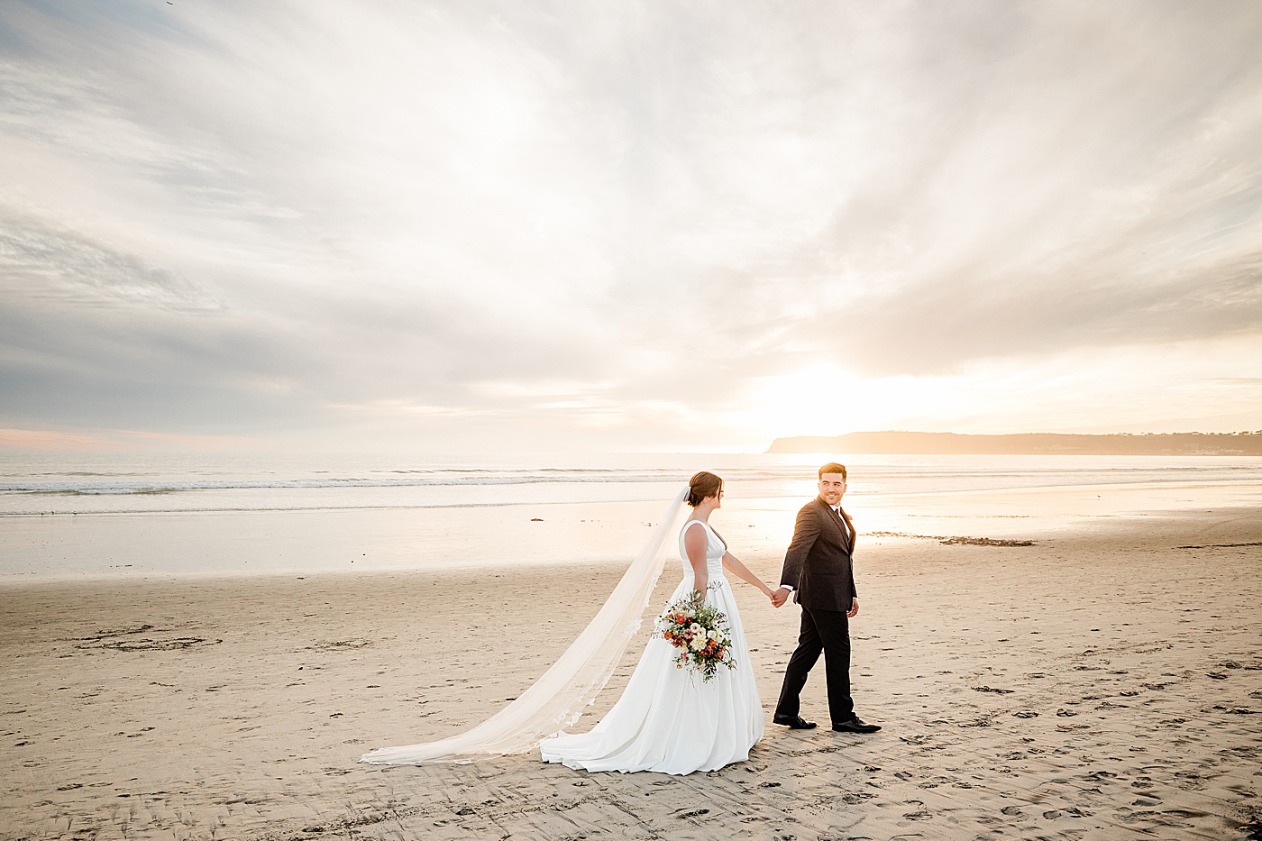 Coronado beach elopement at sunset. Bride and groom walking along the beach.