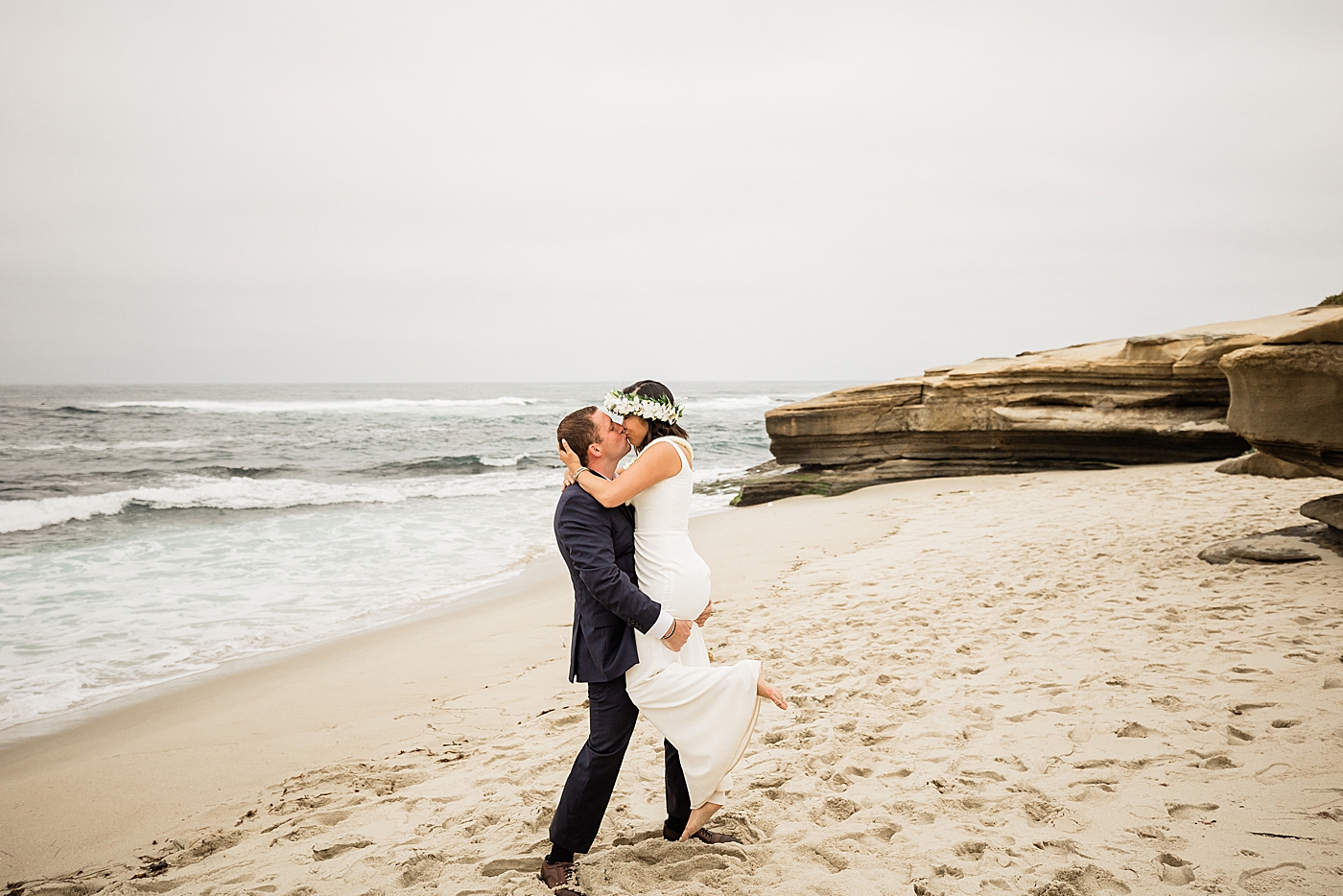 Groom lifting bride up for a kiss on the beach in San Diego elopement.