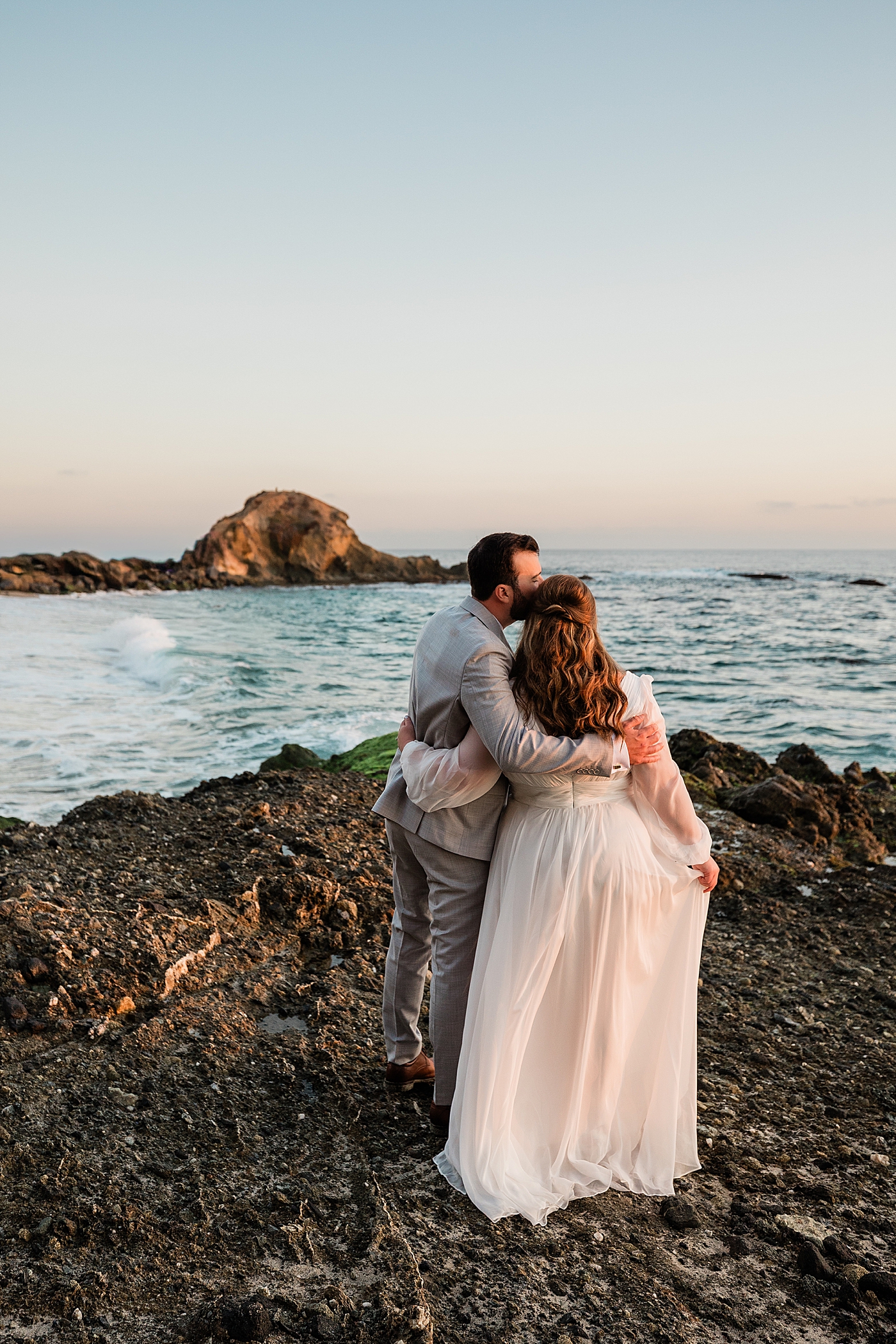 Groom kissing bride facing the sunset in Orange County elopement.