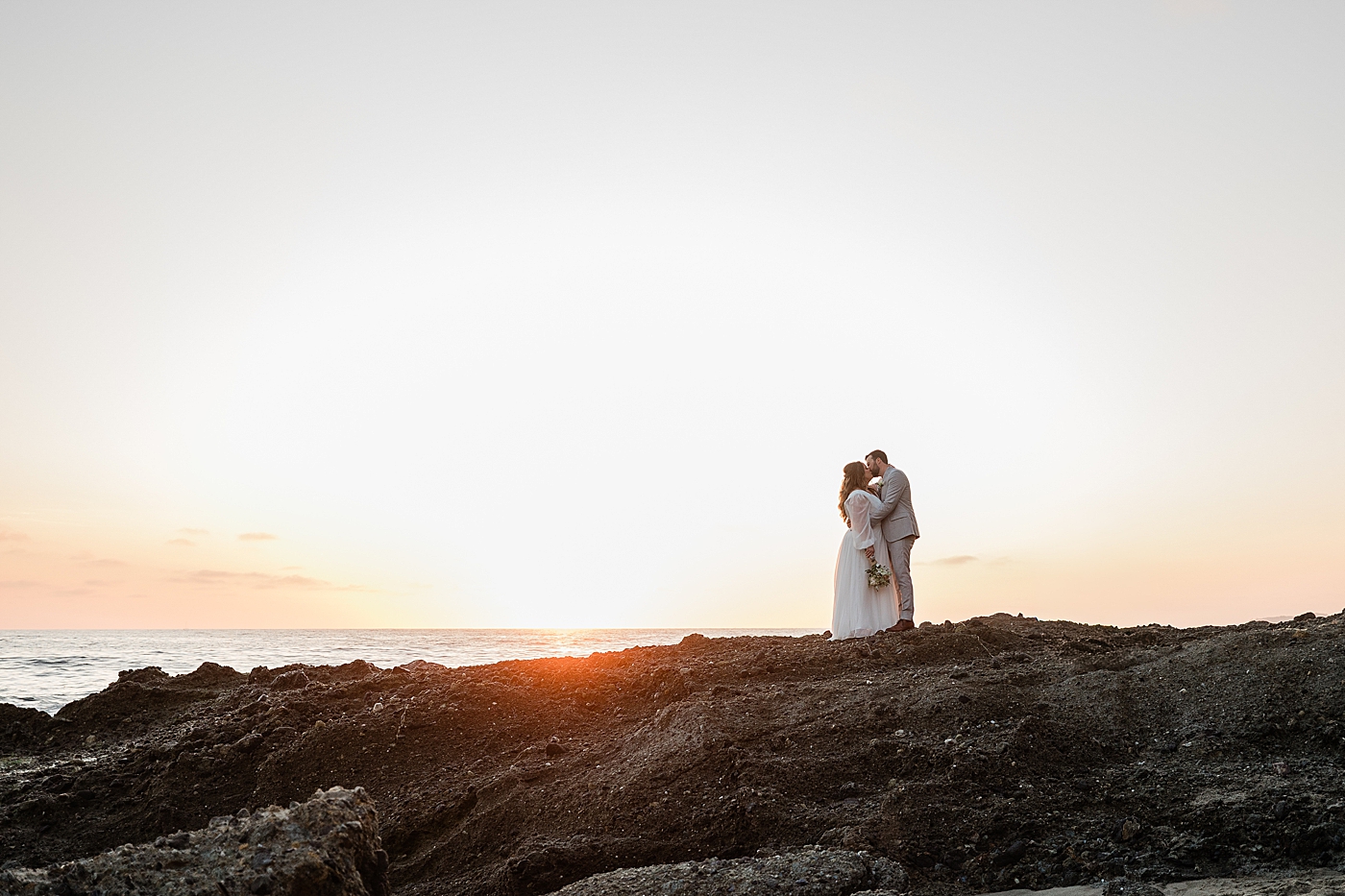 Bride and groom kiss in front of the sunset in Orange County elopement.