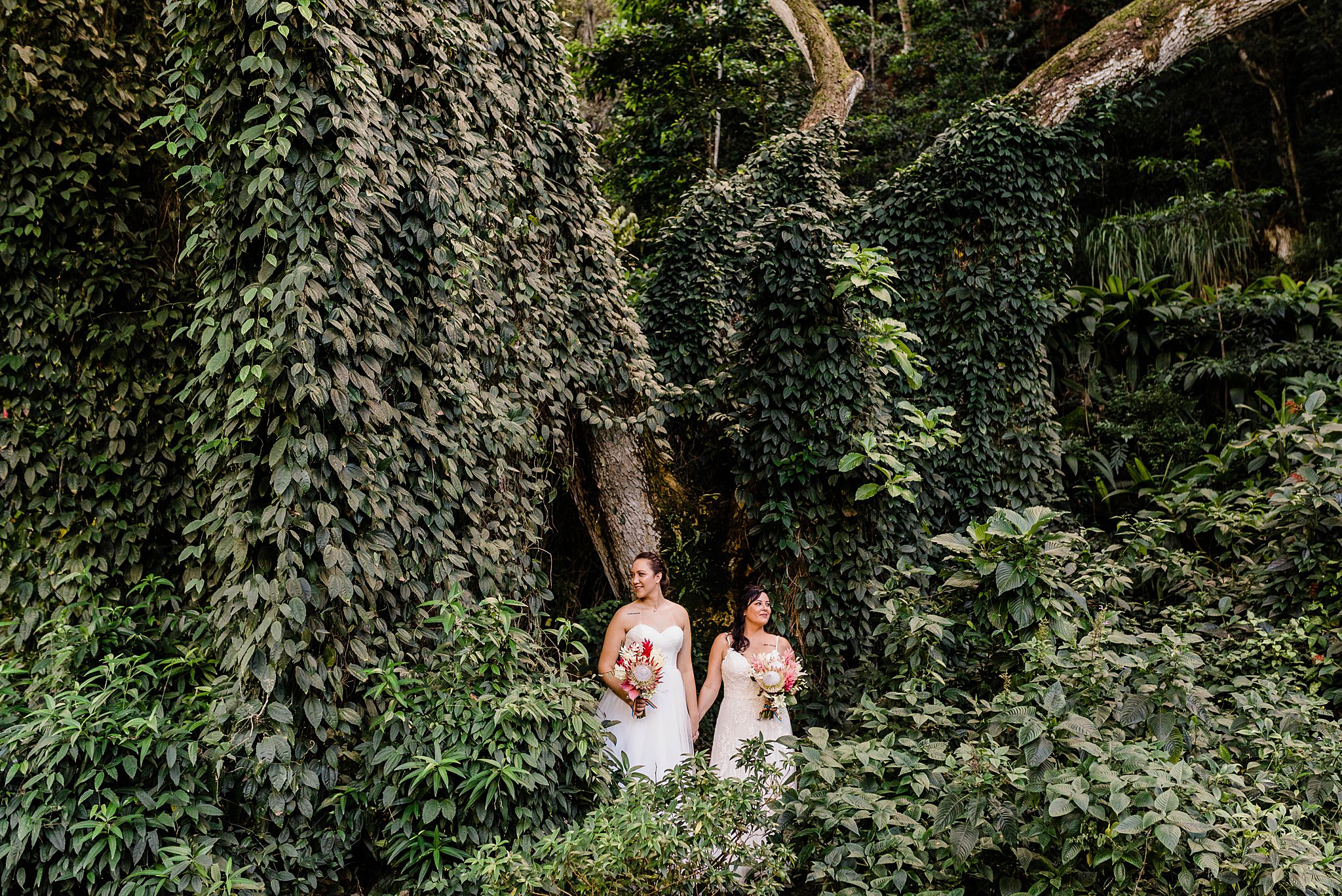 Brides in wedding dresses holding tropical bouquet inside Waimea Valley