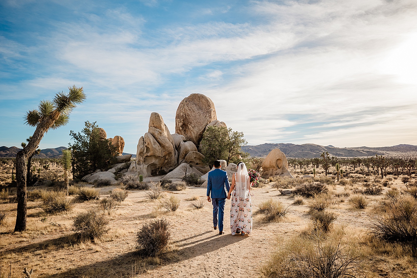 Joshua Tree elopement. Bride and groom walking toward rock formation.
